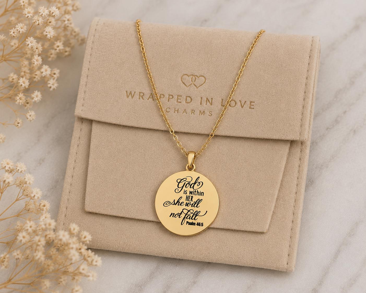 May include: A gold-colored necklace with a circular pendant featuring the inscription "God is within her she will not fall" and "Psalm 46:5". The necklace rests on a beige pouch with the text "Wrapped in Love Charms".
